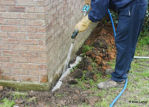 A pesticide technichian applies a termite treatment around a home foundation.