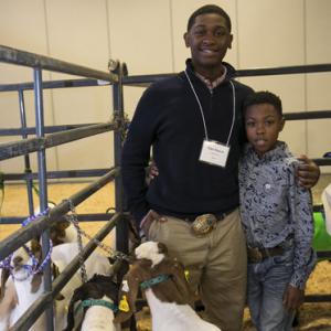 A teenage boy stands next to a young boy while a brown and white goat stands in front of them.