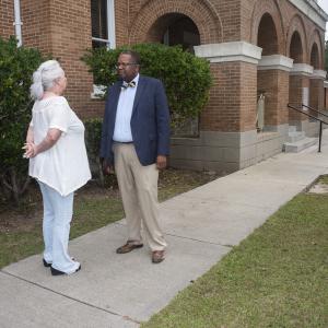 A Black man talking with a white woman in front of a brick building.