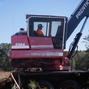 A man sitting in the cab of a tree logger in a cleared field.