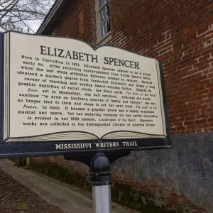 A Mississippi Writers Trail sign about Elizabeth Spencer of Carrollton beside an old brick building.