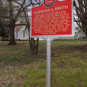 A Mississippi Country Music Trail sign about Narmour & Smith in a pasture near a housing development.