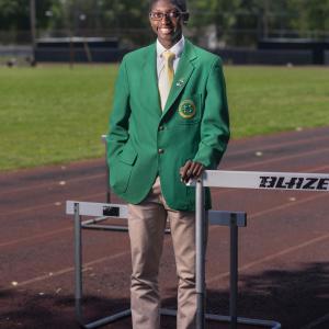 A young man wearing a green 4-H blazer stands smiling on a running track.