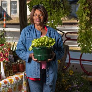 A woman smiling and holding a planter full of lettuce.
