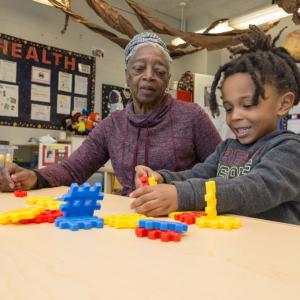 A woman looks on as a young boy plays with shapes.