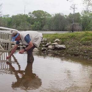 A man collects a water sample at a boat ramp.