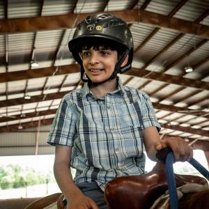 A smiling young man astride a horse and wearing a helmet.