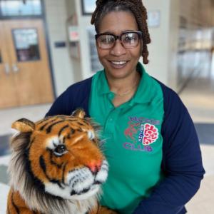 A woman wearing a green polo and a blue sweater hugging a plush tiger.