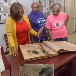 Three woman review an old scrap book, and the inset shows an old photograph of the lady in the center.