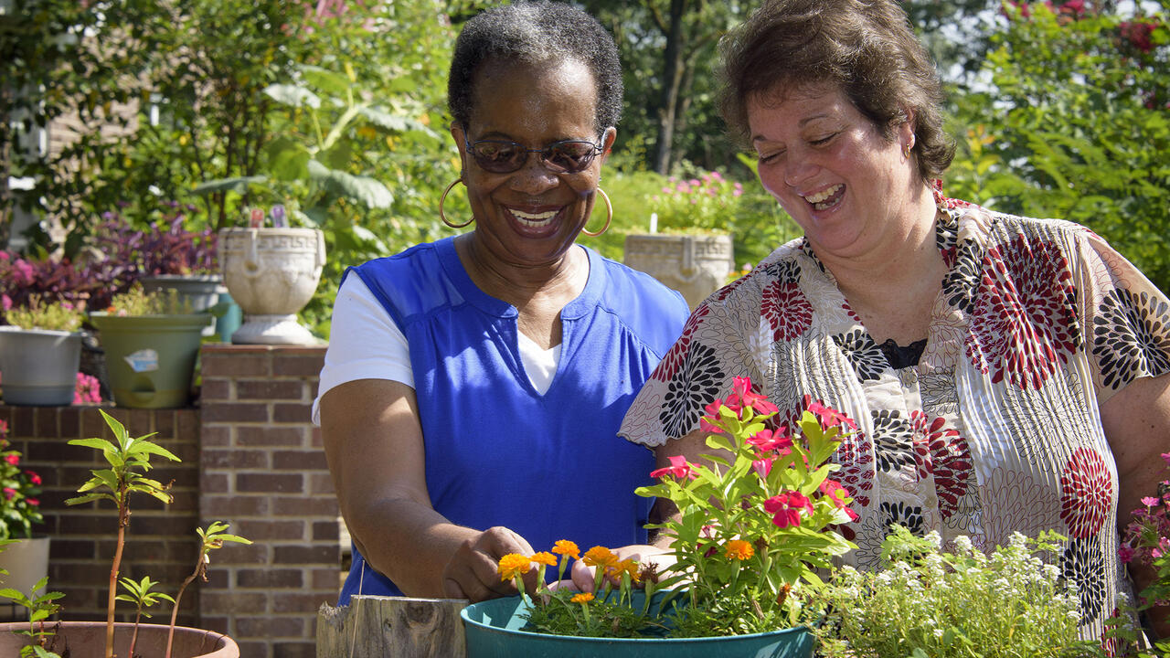 Two women smile as they enjoy colorful potted ornamental plants.