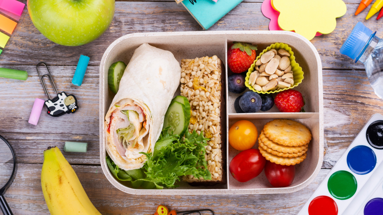 School lunchbox packed with nutritious foods surrounded by colorful school supplies