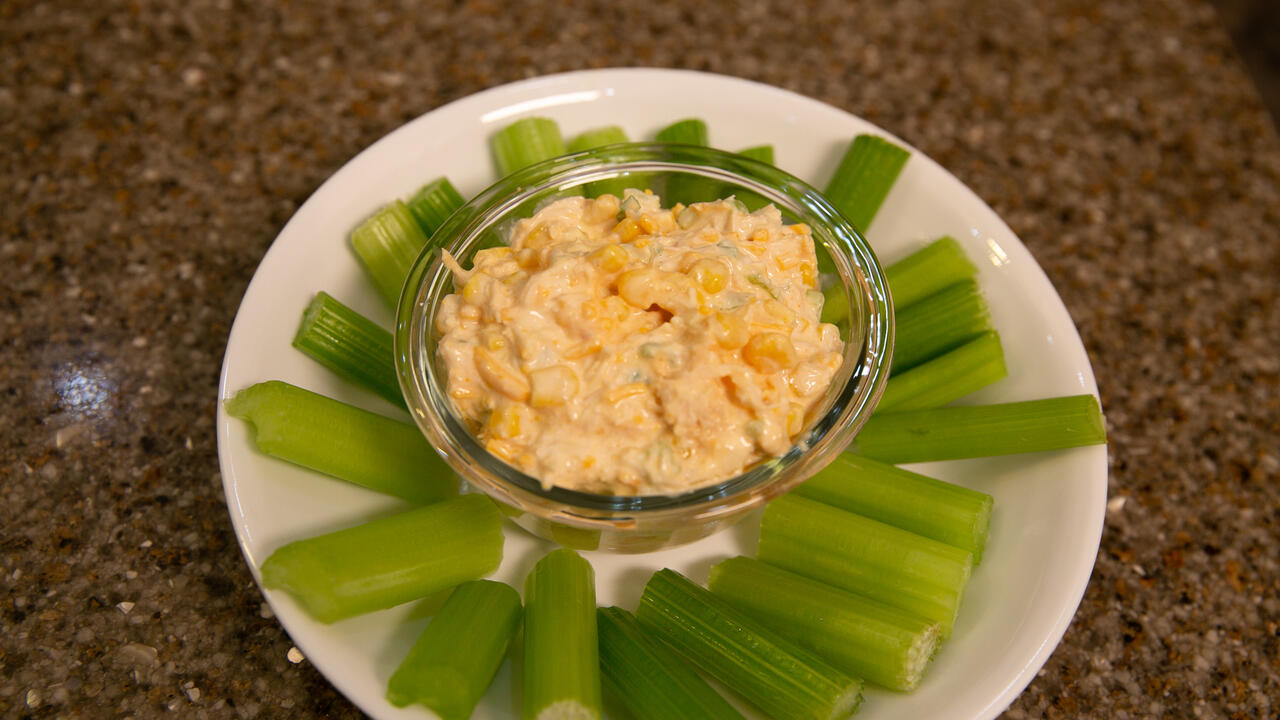 a bowl of Buffalo Chicken Dip stis on a plate surrounded by celery stalks