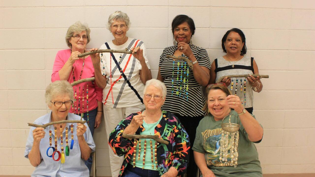 Seven women smile as they hold beaded windchimes.