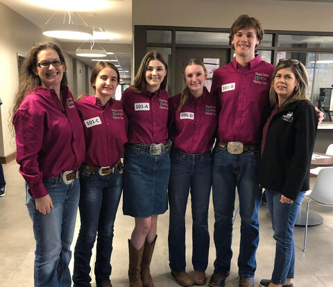 Six people, including two women, three girls, and one boy, wearing maroon polo shirts and smiling at the camera.