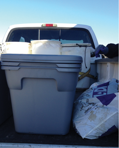 A pickup truck bed with plastic storage bins and a bag of absorbent material.