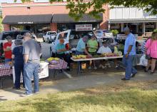 Several people gather to buy produce on display at a farmers market.