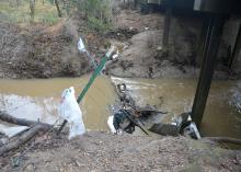 A drainage ditch with moving water, limbs, and trash.