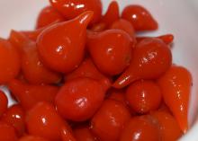 A white bowl is filled with shiny, red peppers that are round shaped with a small point.