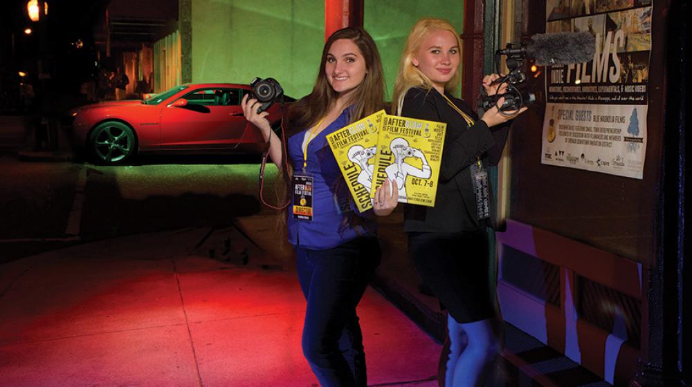 Two teenage girls holding cameras and yellow posters.