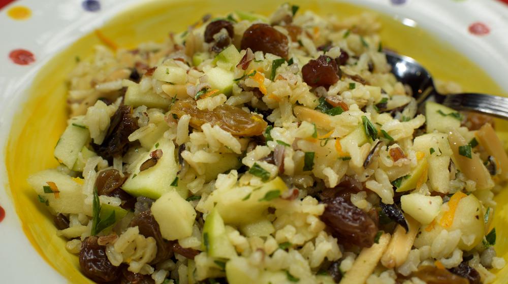 A mixture of rice, apples, raisins and almonds is displayed in a colorful bowl.