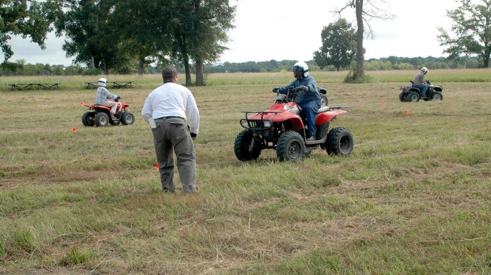 Three young people drive ATVs on a marked course in a field during a safety training.
