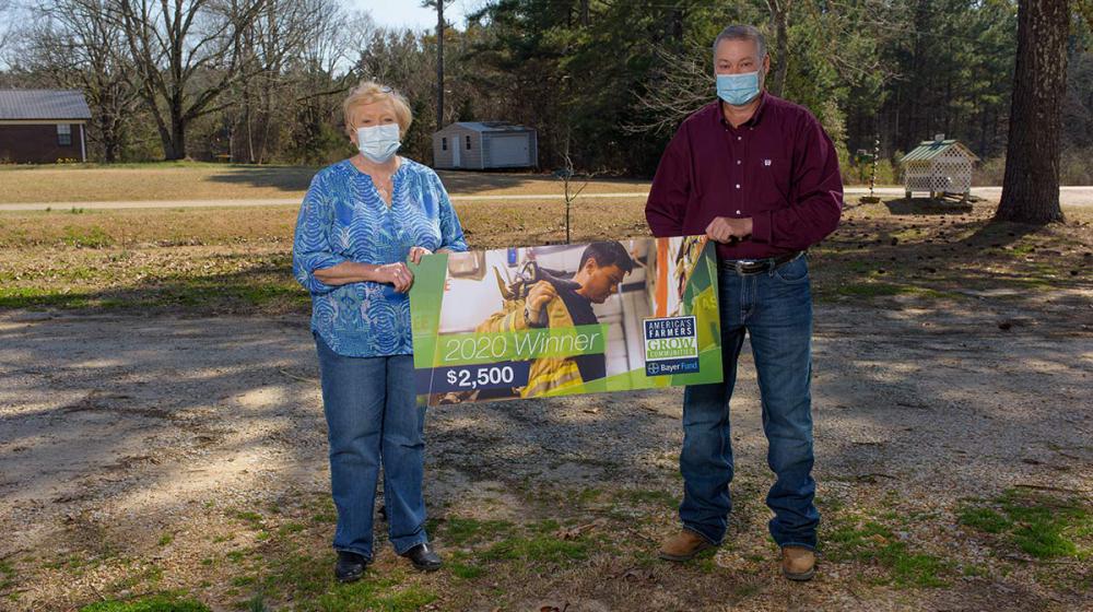A man and woman wearing masks hold each side of a banner that reads “2020 Winner $2,500.”