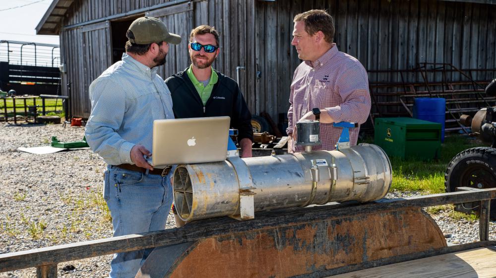 Three men stand around a trailer that holds a large irrigation pipe.