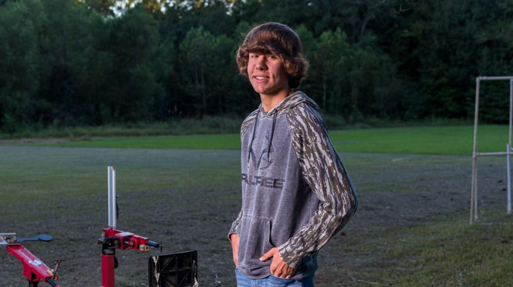 A boy standing beside a sport shooting range smiling.
