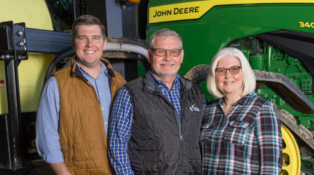 Two men and one woman standing in front of a green tractor