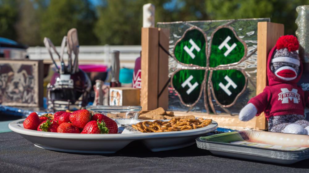 A plate of strawberries and pretzels beside a glass 4-H emblem.