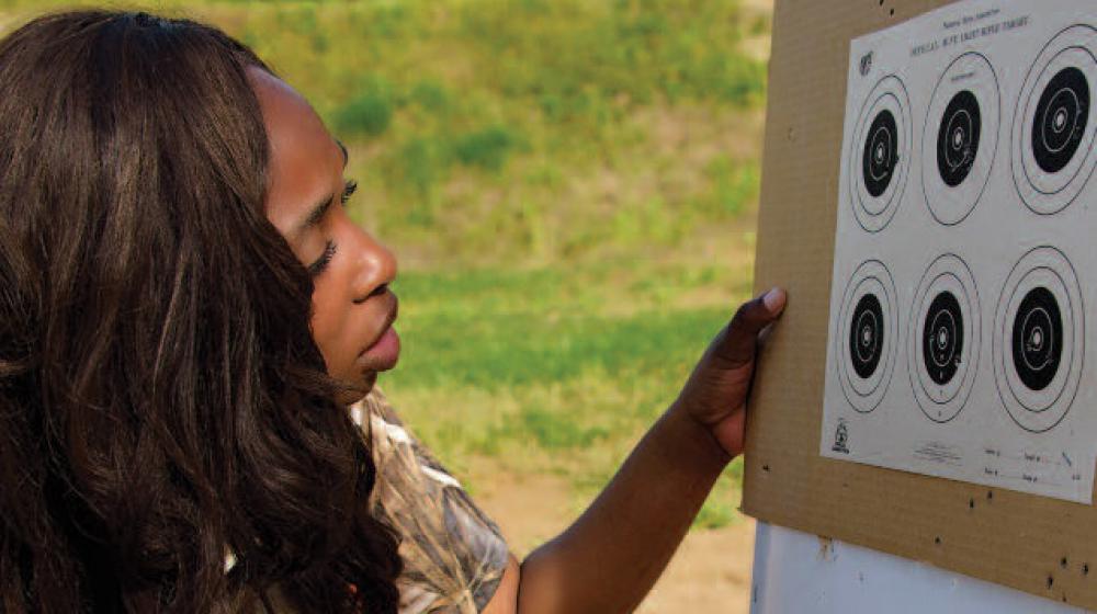 A young woman kneels down next to a board with targets.