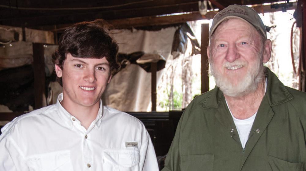 An older man and a young man stand next to each other smiling.