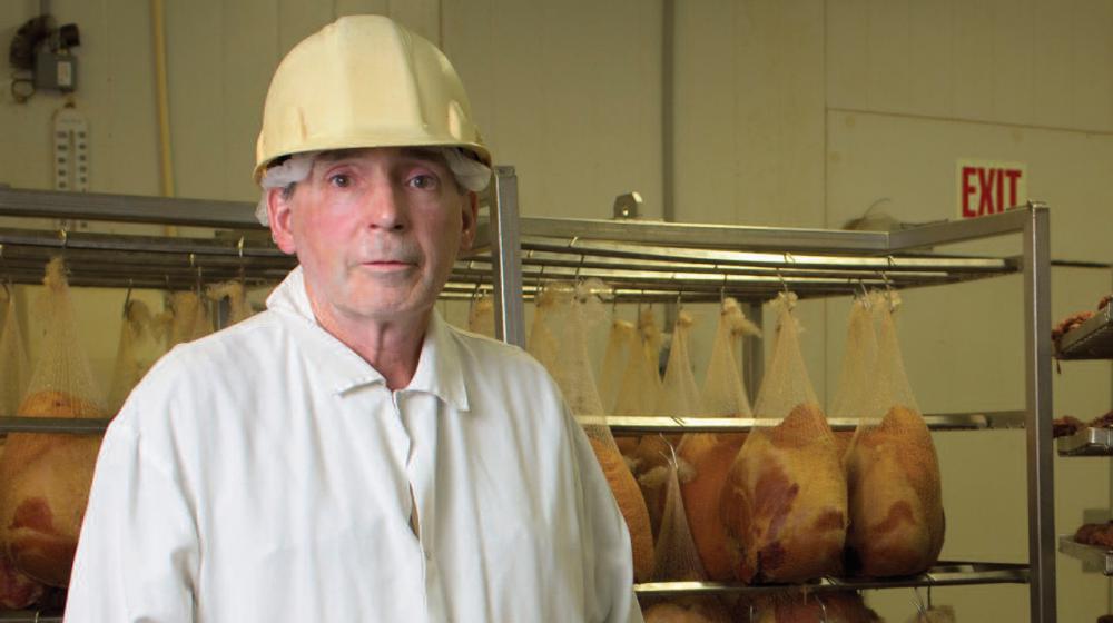 A man stands in front of a rack holding meat.