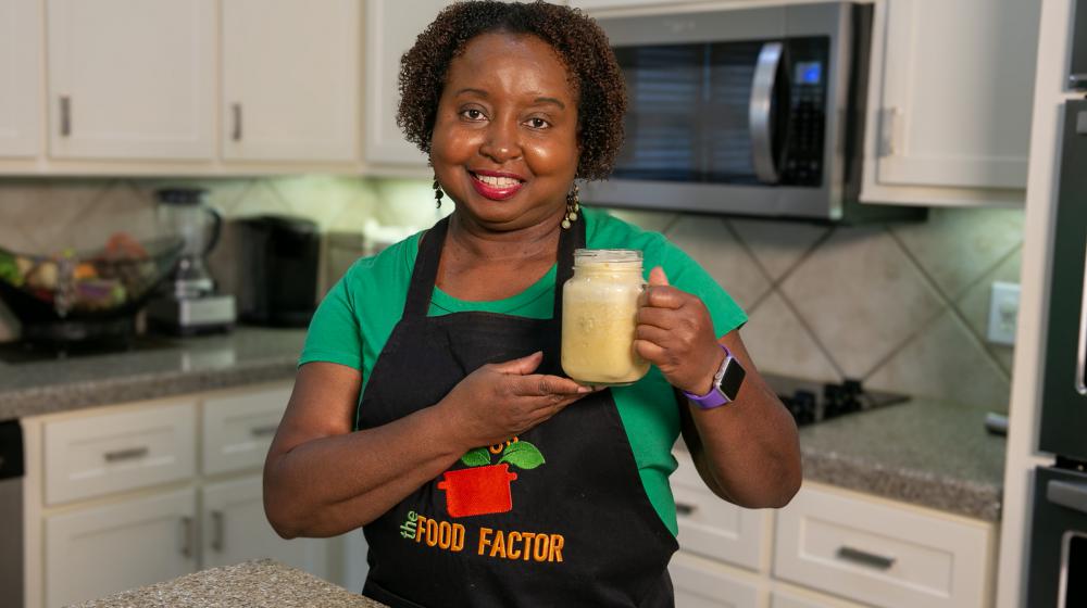 A woman stands in a kitchen holding a glass of peach cooler for the camera.