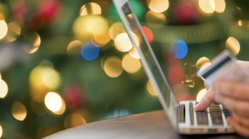 Close up view of a person ordering merchandise from a laptop computer in front of a Christmas tree.