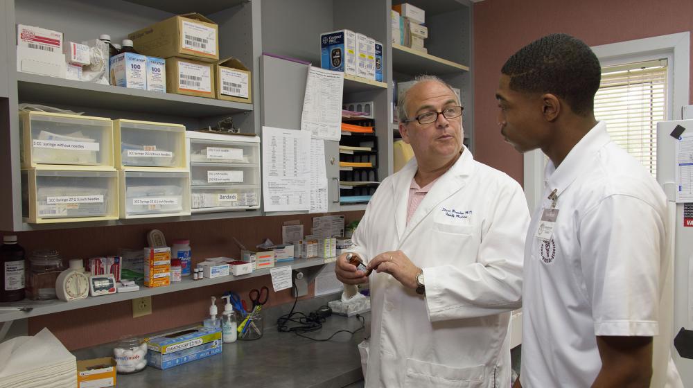 A medical doctor holds a vile of medication and talks to a young man in the Rural Medical and Science Scholars program.