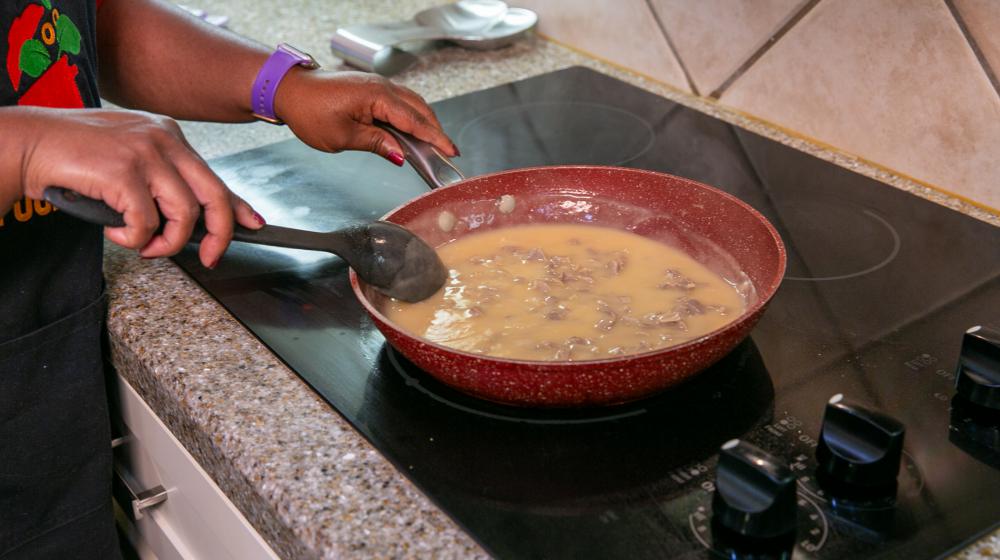 A person stirs a skillet of turkey gravy cooking on the stove.