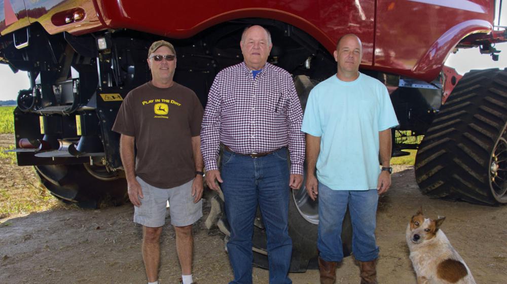 Three men and a dog stand in front of farm equipment.