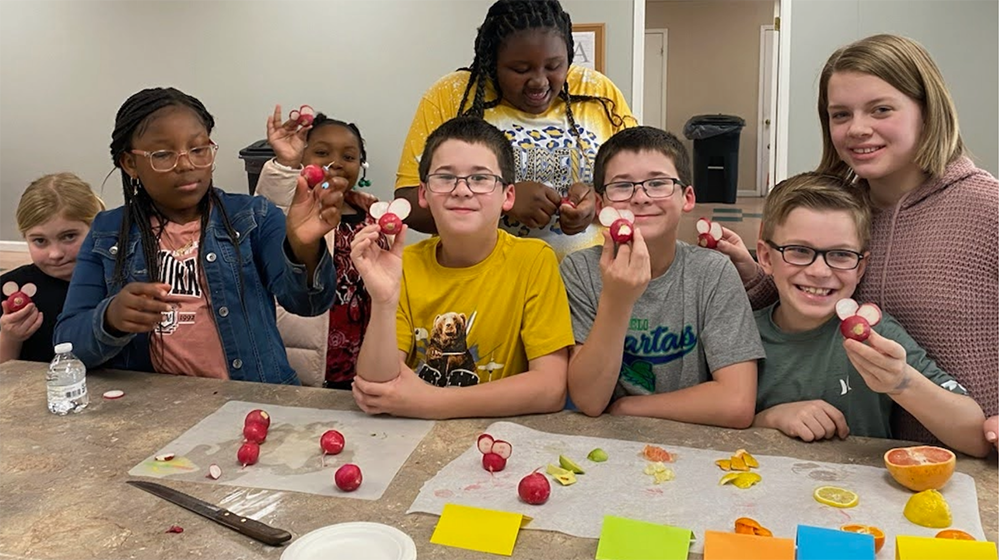 A group of young people standing at a table showing decorative items they made by slicing beets.