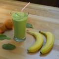 A green smoothie fills a tall clear drinking glass and has a red and white striped straw in it.  