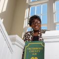 A woman standing behind a green sign that reads "Oktibbeha County 4-H."