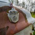 The front of an old Ford truck with the logo centered in an orange-colored rusty area of the light blue truck. 