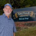 A man stands in front of a sign that reads, “Saltillo Mississippi, Welcome Home.”