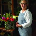 Woman with glasses stands smiling beside a flower arrangement