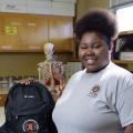 A smiling teenage girl standing next to a black backpack.