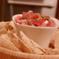Homemade pico de gallo in a white container placed in the center of a wooden bowl of tortilla chips.