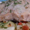 A steamed salmon filet sprinkled with onions and dill sits atop roasted vegetables. 