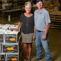 A man and woman stand next to a crate stacked with boxes of sweet potatoes.