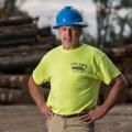 A man, smiling, wearing a hard hat and neon shirt with L&S Logging printed on it.