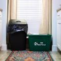 A green recycling bin sitting next to a black trashcan. 